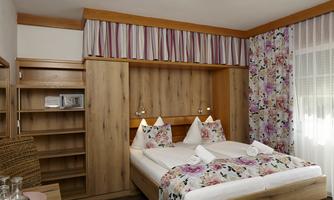 A cozy bedroom with two beds and floral patterns. The wood paneling and the light curtain create an inviting atmosphere.