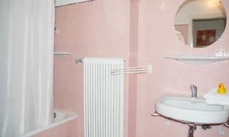 A bathroom in soft pink tones with a bathtub and a shower. A round mirror above the sink and a towel holder complete the furnishings.
