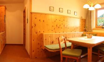A cozy kitchen with wooden paneling and a dining table. The room is bright and friendly with a view of the landscape through the window.