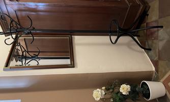 A metal coat rack stands next to a mirror. Next to it is a pot with decorative white flowers.