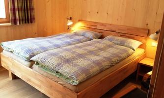 A cozy bedroom with a double bed and wooden interior. The bed linen is checked and the walls are made of light wood.