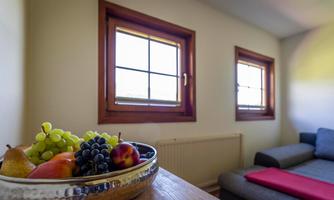 A cozy room with two windows and a gray sofa. On a table, there is a bowl of fresh fruits.