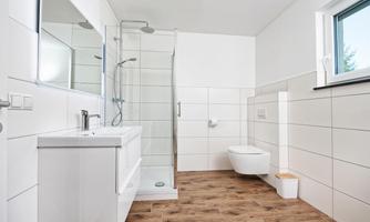 A modern bathroom with a shower, a sink, and a toilet. The walls are covered in light tiles, and the floor is made of wood.