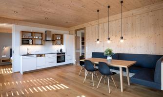 A modern kitchen with high-gloss white cabinets and a dining table for four people. The room has wooden ceilings and a bright, welcoming ambiance.