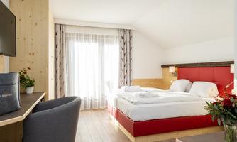 A modern bedroom with a large bed and wooden details. Bright curtains let in plenty of daylight.