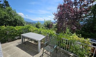 A beautiful outdoor area with a table and a chair.  
Surrounded by green plants and trees, under a clear blue sky.