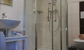 A modern bathroom with a glass shower and a sink. The floor is tiled with dark tiles and there is a small shelf.