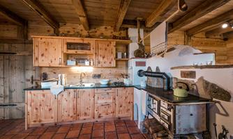 A cozy kitchen with wooden cabinets and a traditional cooking stove. The atmosphere is warm and inviting, with views of rustic materials.