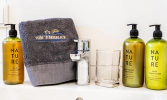 A sink with various care products in green bottles. Below is a towel and a glass.