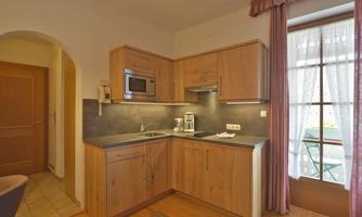 A modern kitchen with wooden cabinets and a countertop. A window provides light and access to a small balcony.