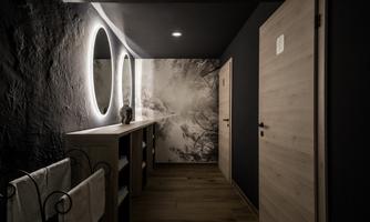 A modern bathroom with warm wood and stylish, dark decor. Soft lighting from round mirrors creates an inviting atmosphere.