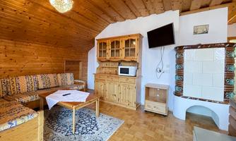 A cozy living space with wooden paneling, a comfortable seating area, and a television. In the background, there is a traditional stove and a small kitchen cabinet.