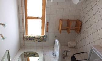 A simple bathroom with white tiles and wooden shelves. There is a shower, a sink, and a toilet.
