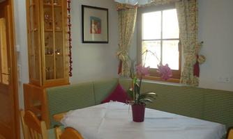 A cozy dining area with a table and chairs. The windows are adorned with curtains, and a flower stands in the center.