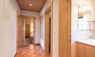 A bright hallway with wooden paneling and terracotta flooring. On the left side, doors to additional rooms are visible.