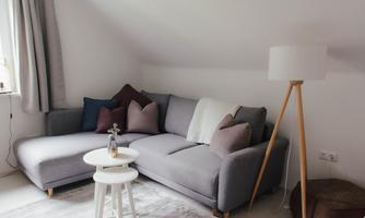A cozy living room with a gray sofa, colorful cushions, and a floor lamp. The room has a bright and inviting atmosphere.