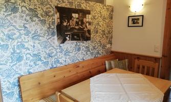 A cozy dining area with a wooden table and benches. The wall is decorated with a blue floral pattern.
