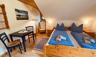 A cozy room with two single beds, a table, and chairs. The warm wood tones and soft lighting create an inviting atmosphere.