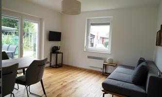 A bright living space with wooden floors and modern furniture. Large windows provide a view of the garden.