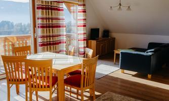 A cozy living room with a dining area and plenty of natural light. The furnishings are made of wood and offer a pleasant atmosphere.