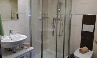 A modern bathroom with a glass door shower and a sink. The walls are tiled in light colors and there is a towel holder.