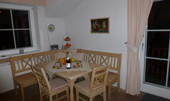 A cozy dining area with a round table and a bench. Fruits and a bottle of sparkling wine are on the table.