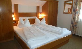 A cozy bedroom with a double bed and wooden wardrobes. The room has natural light and a relaxing atmosphere.