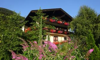 A picturesque house surrounded by colorful flowers and green trees. The clear blue sky creates an inviting atmosphere.