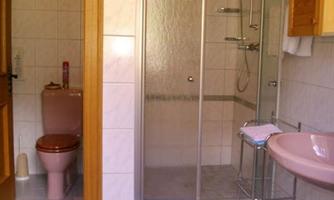 A bathroom with a shower cabin, a sink, and a toilet. The walls are tiled and the room is bright and clean.