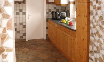 A cozy kitchen with wooden cabinets and a clear workspace. The floor is made of tiled stones and the room has a warm atmosphere.