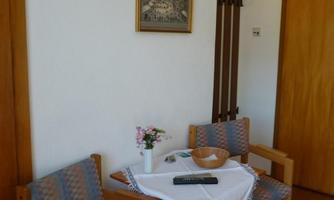 A cozy room with two chairs and a small table. On the table are a vase with flowers and a bowl.