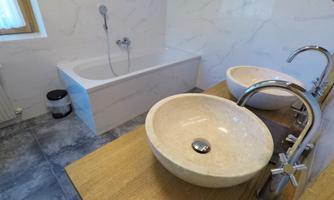 A modern bathroom with a bathtub and two ceramic sinks. The walls are bright, and there are large windows that let in natural light.