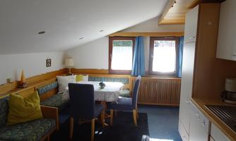 A cozy living area with a dining table and blue chairs. Bright windows provide plenty of daylight in the atmosphere.