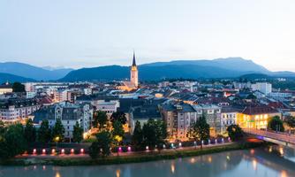 A beautiful city view at dusk with a river in the foreground. The lights of the buildings and the church tower shine in the evening atmosphere.