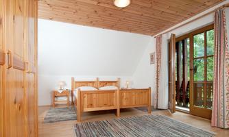 A cozy bedroom with wooden decor and two beds. Large windows offer a view outside and let in plenty of daylight.