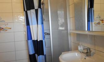 A small bathroom with a shower cabin and a sink. The walls are tiled, and the shower curtain has a blue and white pattern.