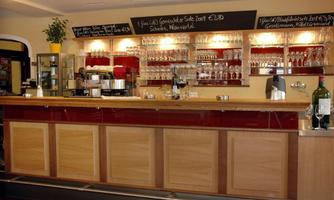 A cozy bar with an elegant wooden counter and shelves full of glasses. On the wall, there are menu boards showcasing offers.