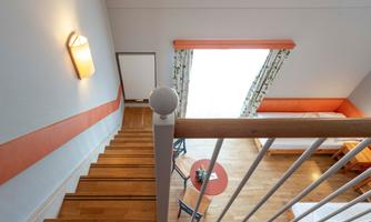 A bright staircase with wooden steps leads to a cozy room. A window with curtains lets in plenty of daylight.
