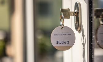A key plate with the inscription "Studio 2" hangs on a door. The key is in the lock and the background shows a bright ambiance.