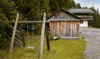 A rustic wooden house surrounded by trees. On the left side, there is a swing.