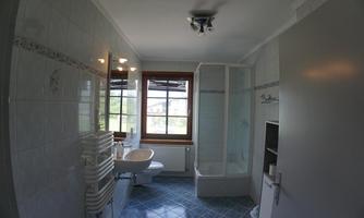 A modern bathroom with a shower, sink, and window. The walls are tiled and the floor is blue.