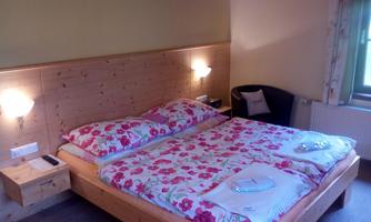 A cozy bedroom with a double bed and floral bedding. The walls are bright, and there is a comfortable seating area.
