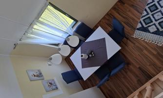 A bright dining area with a white table and blue chairs. Large windows provide plenty of daylight.
