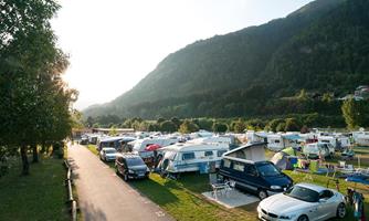 A campsite in a picturesque mountain landscape. RVs and cars are arranged along a road, surrounded by green meadows and trees.
