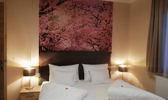 A cozy bedroom with a large bed and two nightstands. A large picture of blooming cherry blossoms hangs on the wall.