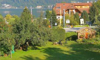A picturesque landscape with a green garden and a charming wooden house. In the background, there are houses and a tranquil lake.