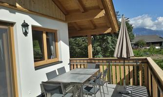 A cozy terrace with a table and chairs. In the background, there are trees and a clear sky.