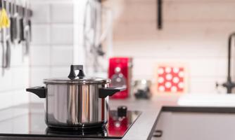 A shiny cooking pot on a modern stovetop in a stylish kitchen. In the background, kitchen utensils and a decorative wall are visible.