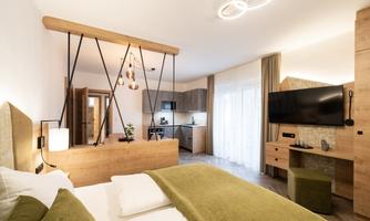 A modern room with wooden details and cozy furnishings. It features a kitchenette and large windows that let in plenty of light.