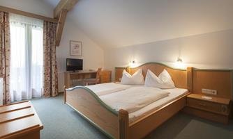 A cozy hotel room with a double bed and two pillows. There is a television and a table as well as a balcony with curtains.